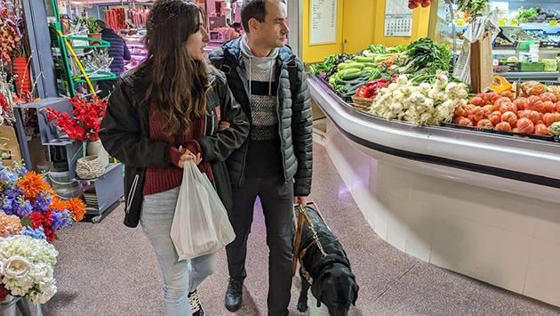 L'afiliat Jordi Salido amb el seu gos pigall i l'educadora del Mercat, Alba Daros, compren en una parada.
