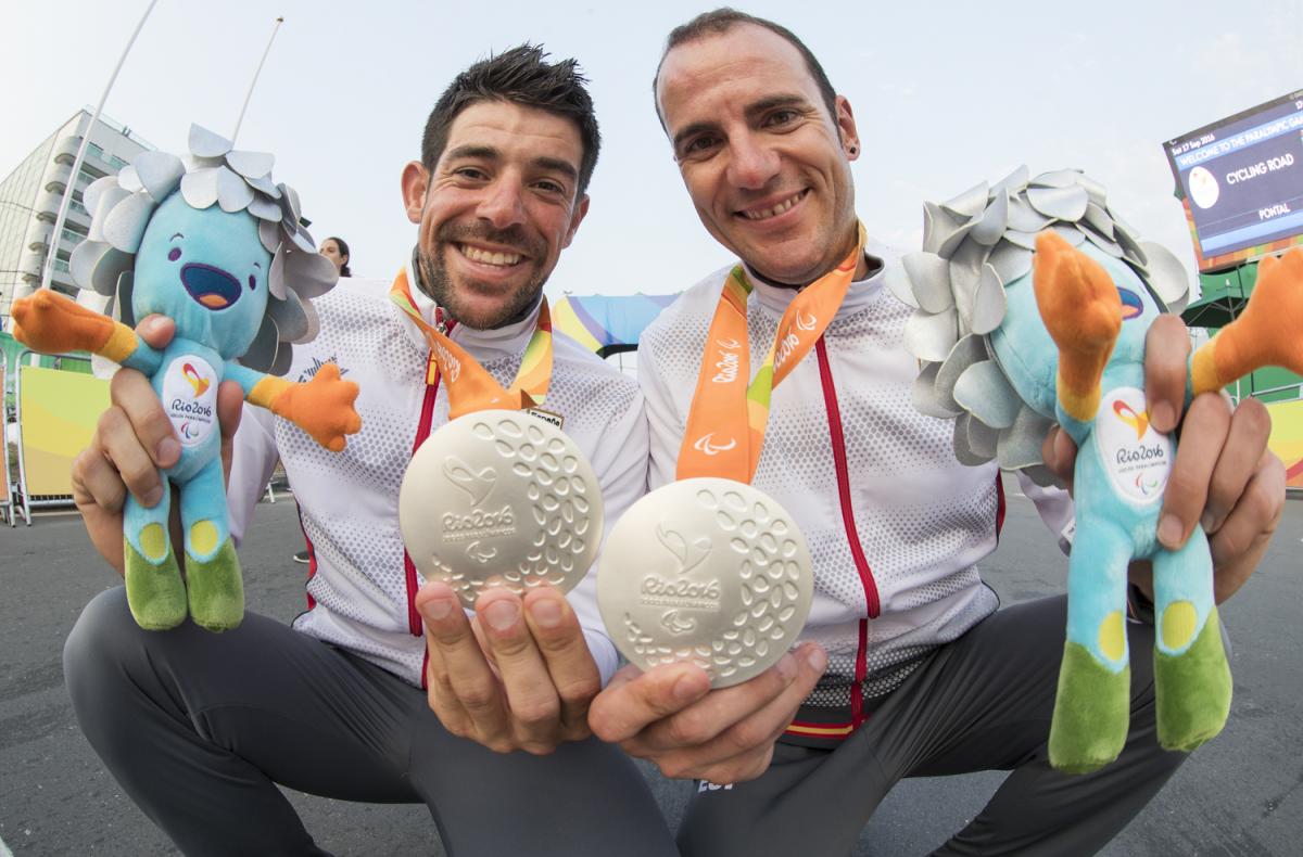 Ignasi Àvila i el seu guia Joan Font, plata a la prova de ciclisme en ruta, mostren somrient  la mascota i les seves medalles.
