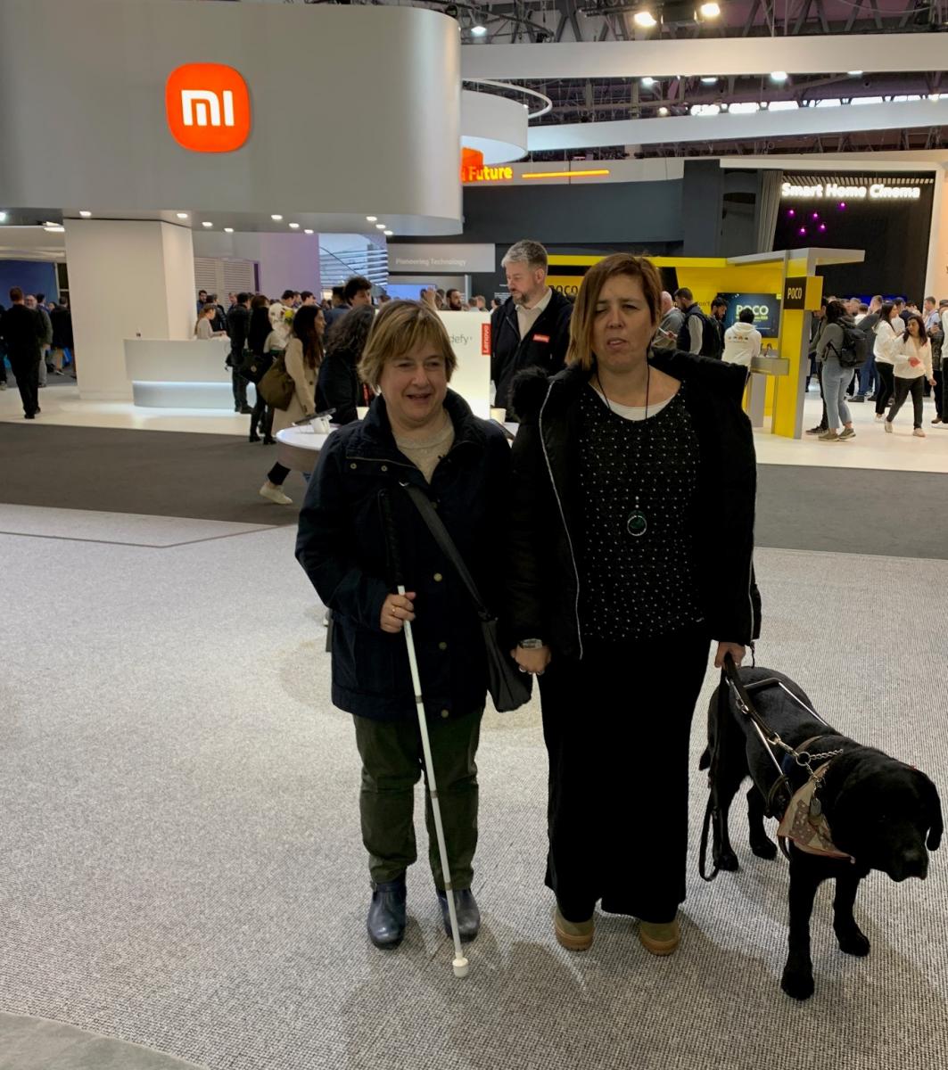 Anaïs Garcia, Cap d'Autonomia Personal de l'ONCE Catalunya, amb la seva gossa pigall Cometa, i l'Anna Andreu, instructora de tiflotecnologia, fent la visita a cegues pel MWC Barcelona 2023