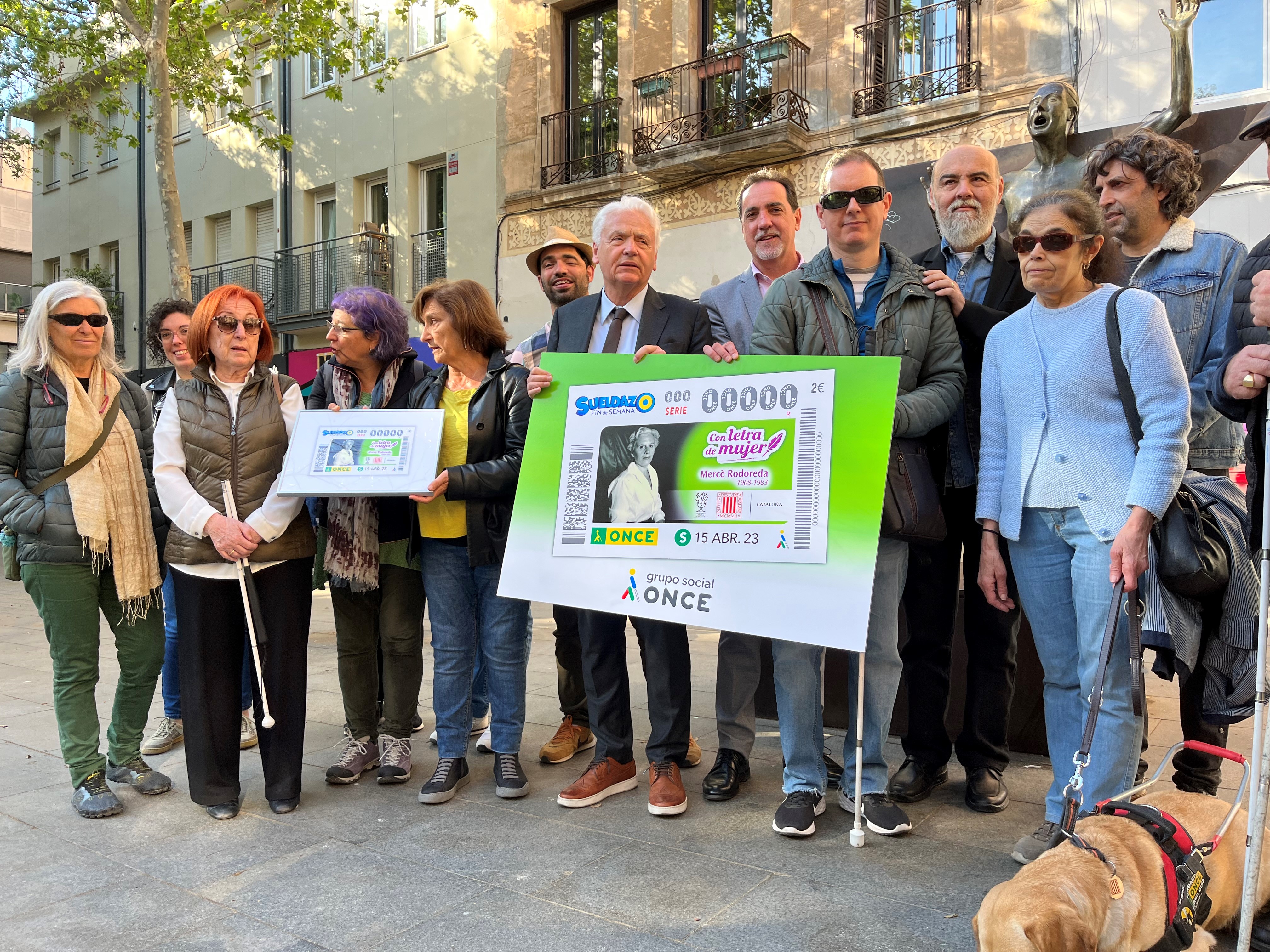 Foto de família, d'afilaits i afiliades i el delegat d'ONCE Catalunya, amb Ferran Mascarell, al monument a 'La Cololometa' mostrant el cupó dedicat a Mercè Rodoreda.