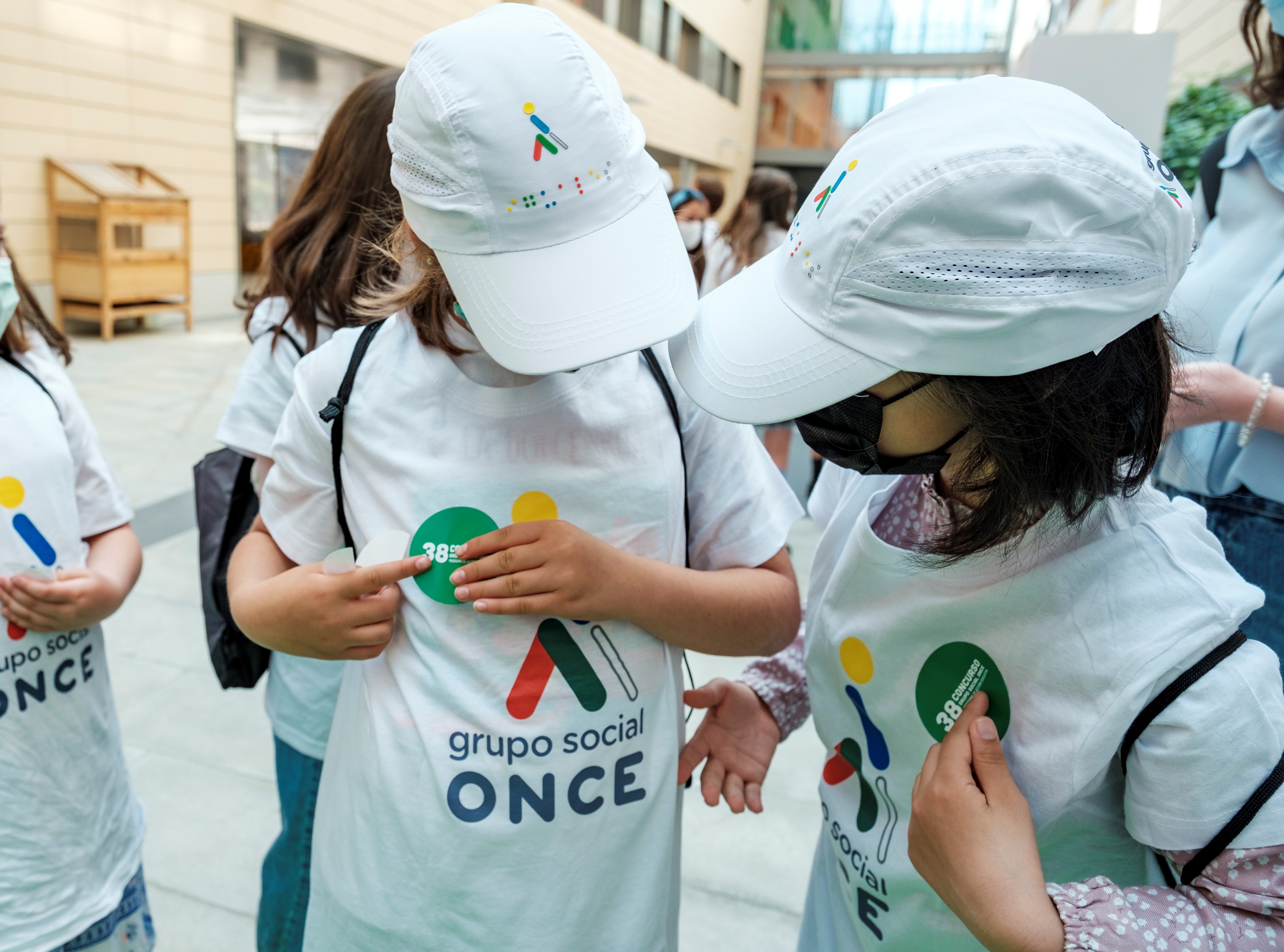 Dues nenes amb gorra i samarreta amb el logo del Grup Social ONCE