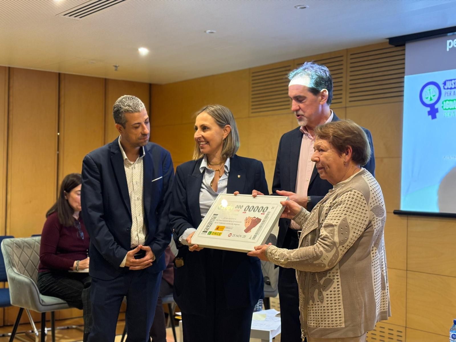 Enric Botí, delegat de l’ONCE a Catalunya, va lliurar a Eva Menor, consellera del Departament d'Igualtat i Feminisme de la Generalitat de Catalunya, el cupó amb el lema ‘Juntes som més fortes’. També els van acompanyar David Bernardo, president del Consell Territorial de l’ONCE Catalunya, i Mercè Batlle, presidenta del COCARMI. 