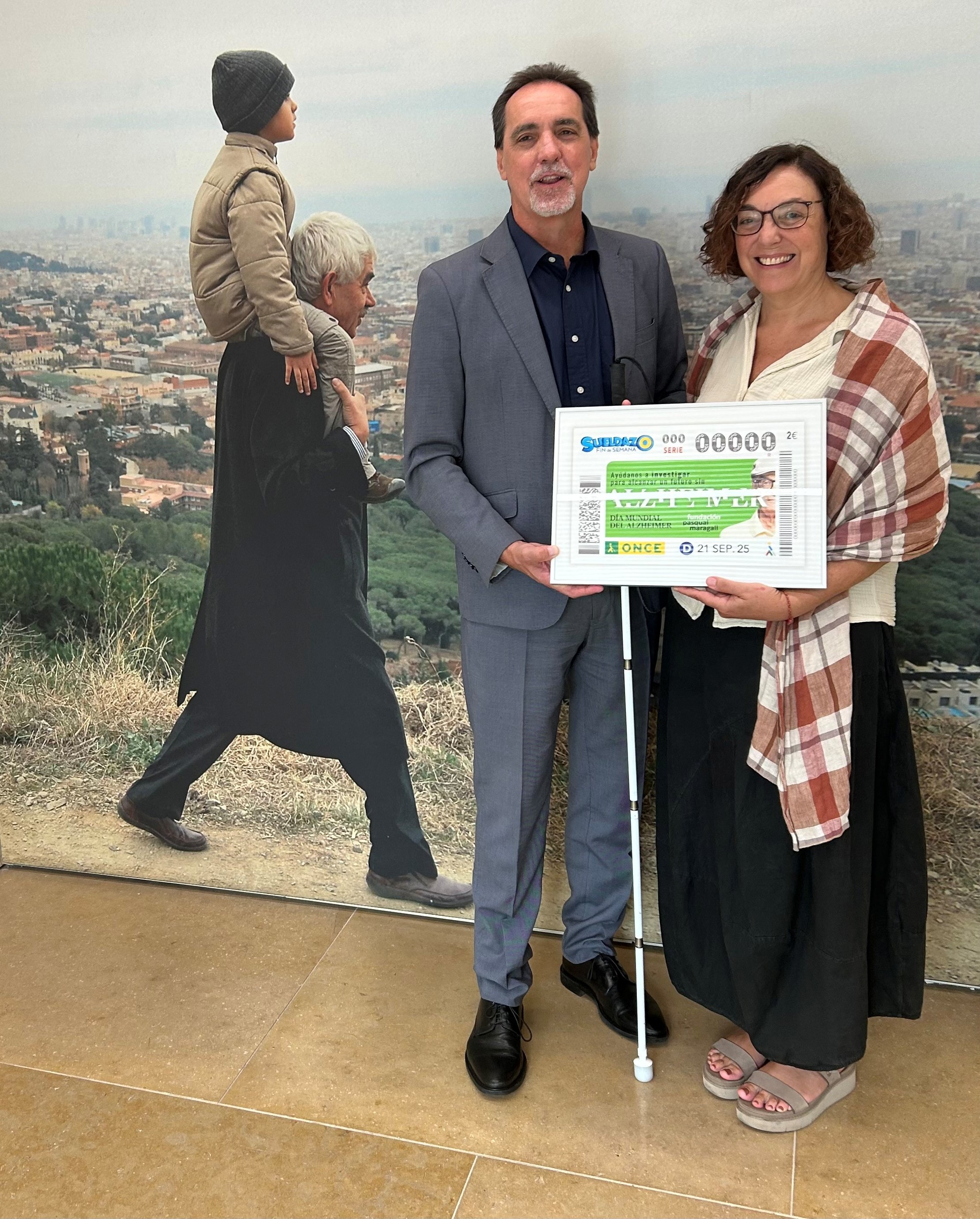 Enric Botí, delegat de l’ONCE a Catalunya, va lliurar a Cristina Maragall, presidenta de la Fundació Pasqual Maragall , una imatge emmarcada del cupó. Darrere una foto de Pasqual Maragall amb el seu net.  
