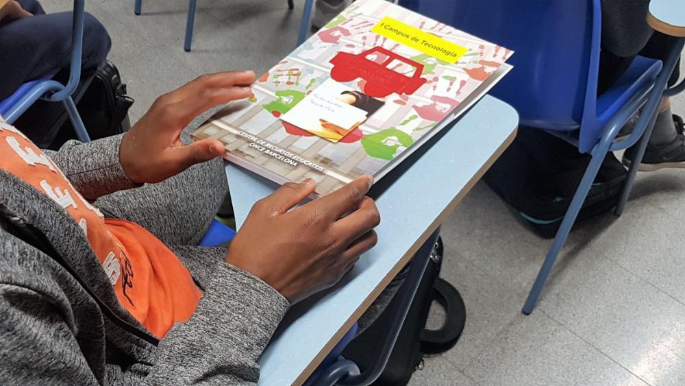 Manos en primer plano de un alumno con el dossier del Campus Inclusiu.