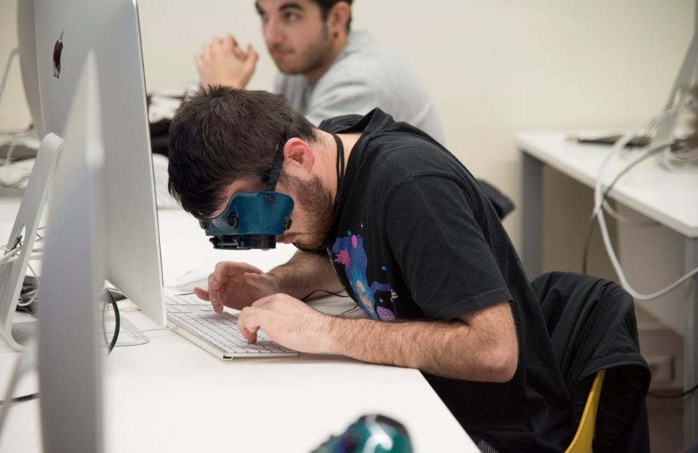 Alunbe de la Universitat de Lleida amb unes ulleres de simulació tracta d'escriure amb el teclat de l'ordinador.