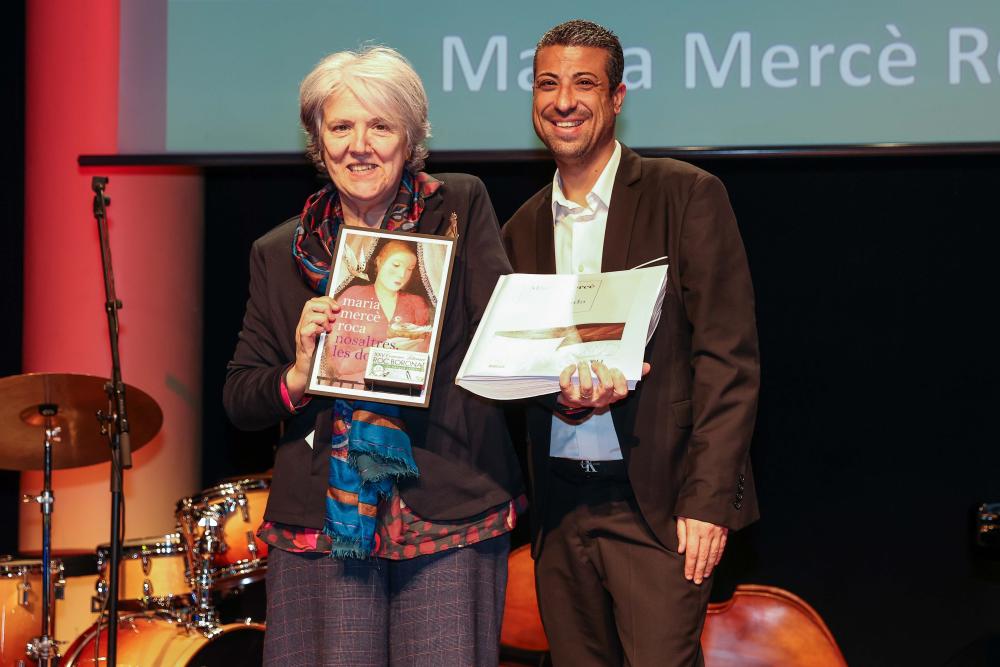 Maria Mercè Roca i David Bernardo, dalt de l'escenari amb un exemplar en braille del seu llibre Temporada baixa i un altre en suport sonor de Nosaltres les dones.  