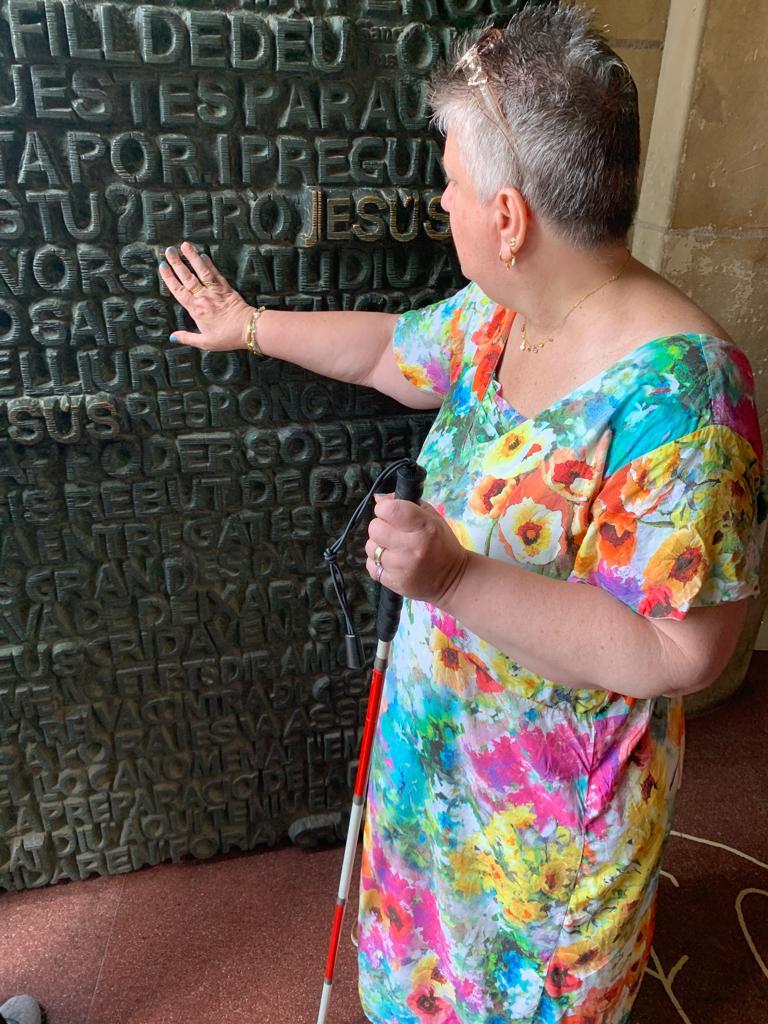 Una dona amb bastó blanc-i-vermell tocant una de les parets de la Sagrada Família