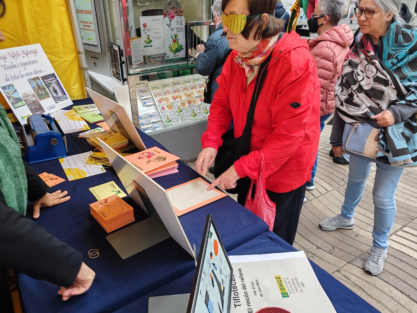 Una dona amb antifaç llegeix un conte en relleu a l'stand de l'ONCE a La Rambla de Barcelona.