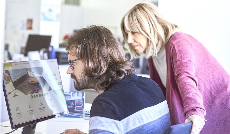 Dues persones dvant pantalla ordinador, una d'elles amb discapcitat visual.
